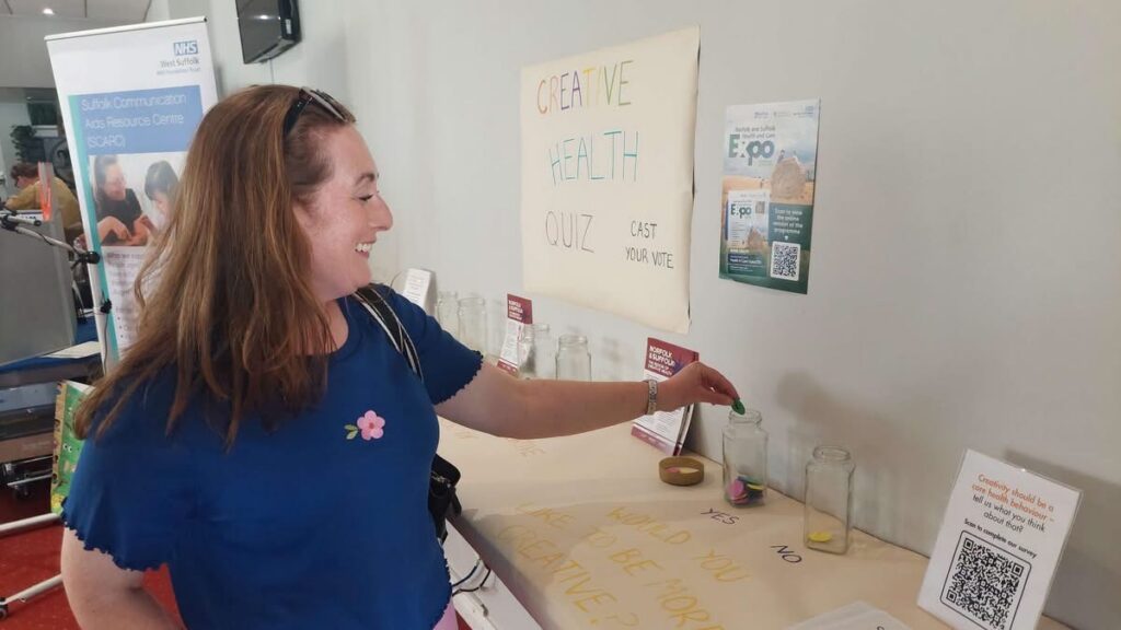 Woman putting a voting token in a glass jar in the Creative Health area