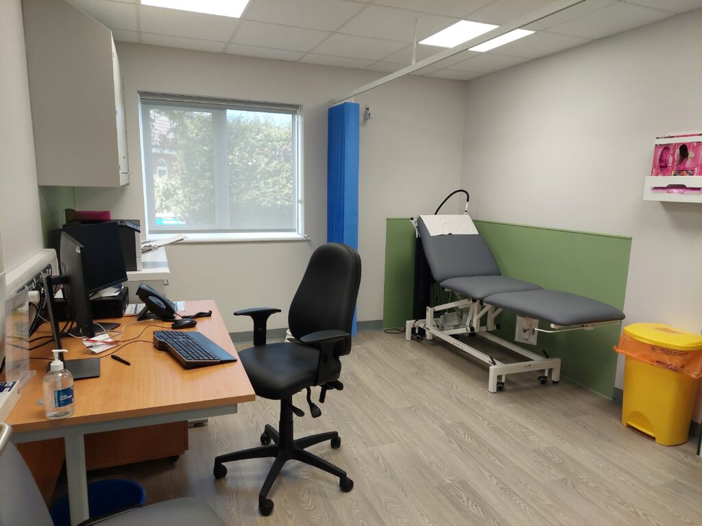 Newly opened medical consultation room with desk, bed and privacy curtain.