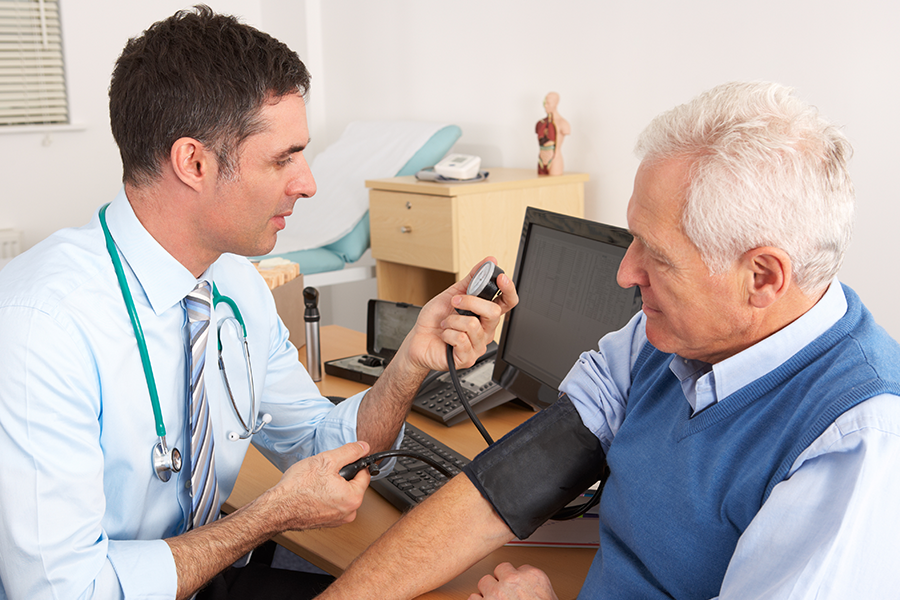 An older man is getting his blood pressure taken by a clinician.