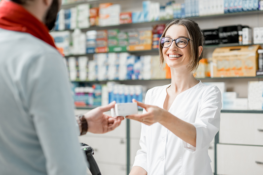 Smiling pharmacist hands medication to a customer.
