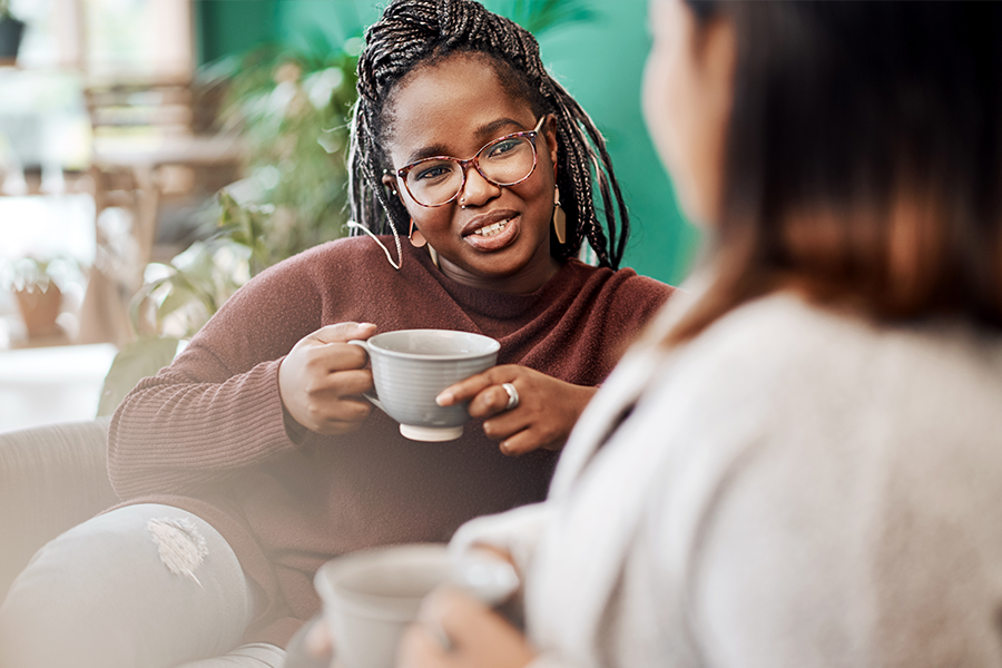 A young woman holding a coffee mug. She is talking to a friend.