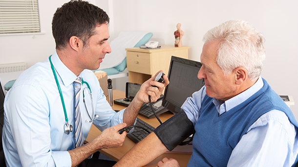 An older man is getting his blood pressure taken by a clinician.