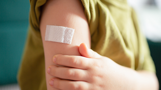 A person in a green t-shirt with one sleeve rolled up is holding their arm. They have a small plaster just below their shoulder,