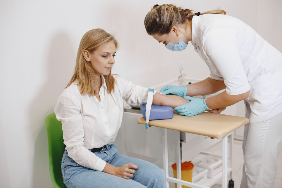 Woman sits while a nurse stands and takes bloods from her arm,