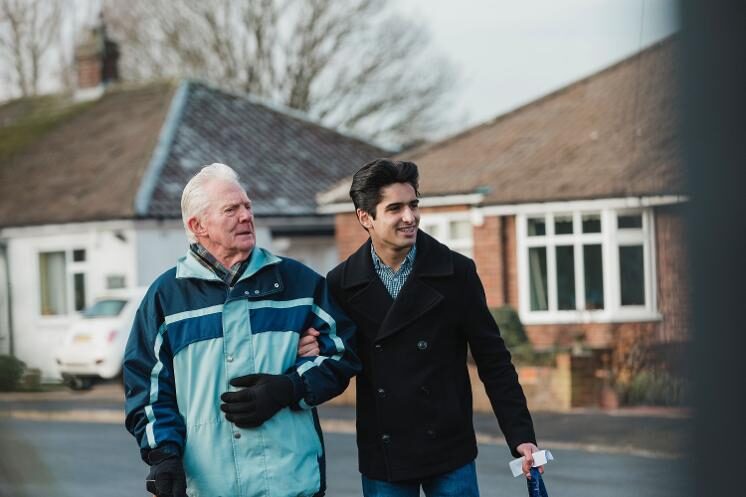 Man helping older man cross the road in a residential area